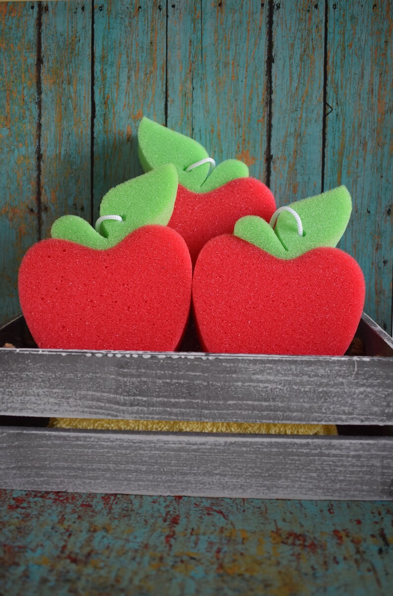 May include: Three red sponge apples with green leaves in a gray wooden crate. The crate is sitting on a blue and green wooden surface.