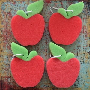 May include: Four red apple-shaped bath sponges with green leaf accents. The sponges are made of a soft, textured material and are perfect for cleaning and exfoliating.