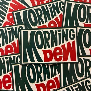 May include: A stack of green and red stickers with the words "MORNING DEW" in a stylized font. The stickers are printed on white paper.