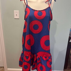 May include: A blue sleeveless dress with a red donut pattern. The dress has a ruffled hem and thin straps that tie at the shoulders.