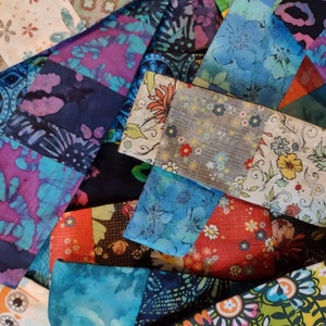 May include: A close-up of a patchwork of fabric pieces in various colours and patterns. The fabrics feature floral, paisley, and abstract designs in shades of blue, purple, red, and green. The pieces are arranged in a geometric pattern.