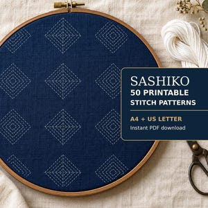 May include: A round wooden embroidery hoop containing dark blue fabric with white stitched diamond patterns. A dark blue rectangular label displays the text: SASHIKO 50 PRINTABLE STITCH PATTERNS A4 + US LETTER Instant PDF download. White thread and scissors are present.