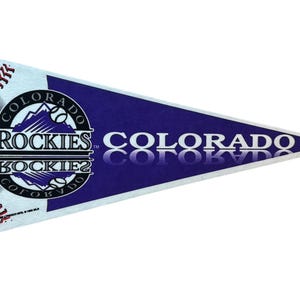 May include: A triangular pennant featuring the Colorado Rockies logo. The pennant has a dark blue background with the words "COLORADO" in white. The Rockies logo includes a mountain range and baseballs.