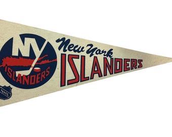 May include: A triangular felt pennant in off-white featuring the New York Islanders logo in blue and orange. The design includes a hockey stick, a puck, the text New York Islanders, and a small NHL shield logo in the lower left corner.