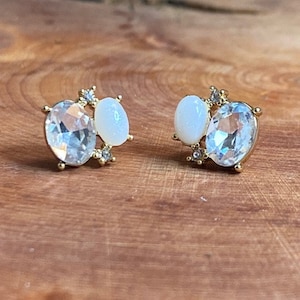 May include: A pair of gold earrings with two oval-shaped stones. One stone is clear and the other is white.