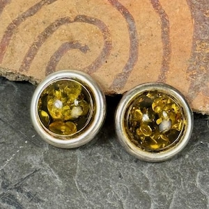 May include: A pair of silver earrings with round amber stones. The amber is a dark yellow color with flecks of gold and white.