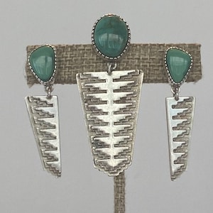 May include: A set of silver earrings with turquoise stones. The earrings feature a geometric design with a triangular shape.