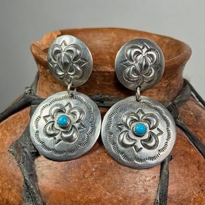 May include: A pair of silver dangle earrings with turquoise stones. The earrings feature a floral design and are a traditional Native American style.