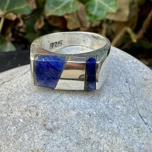 May include: A sterling silver ring featuring two rectangular blue lapis lazuli inlays set into the band. The interior of the band is clearly stamped with the hallmark 925, indicating the silver content of this polished metal jewelry piece.
