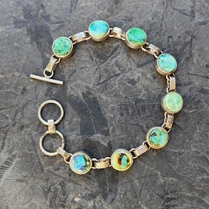 May include: A silver bracelet with a toggle clasp features round green and blue iridescent stones.