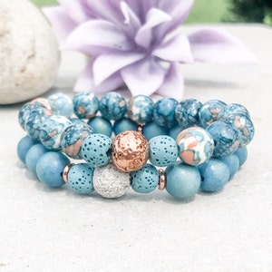 May include: Three stacked bracelets with blue, white, and copper beads. The top bracelet has blue and white patterned beads, the middle bracelet has blue beads with small holes, and the bottom bracelet has solid blue beads.
