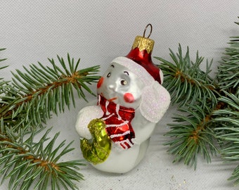 May include: A snowman Christmas ornament with a red hat and scarf, holding a green and gold gift. The ornament has a silver body and white glitter accents. Festive holiday decor.