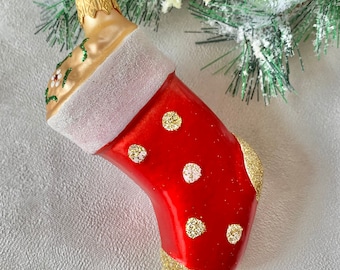Könnte beinhalten: Roter Weihnachtsstrumpf-Ornament mit goldenen Glitzerakzenten und weißen Tupfen. Die Oberseite und die Ferse des Strumpfes sind mit goldenem Glitzer verziert. Das Ornament hat eine goldfarbene Oberseite mit floralen Details und eine silber-weiße Manschette.