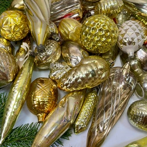 May include: A collection of vintage glass Christmas ornaments in gold and silver tones. The ornaments are various shapes, including balls, teardrops, and cones. Some have intricate patterns and textures.