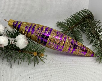 Könnte beinhalten: Ein langer, violetter und goldener Weihnachtsbaumschmuck mit glitzernder Oberfläche. Der Schmuck ist tropfenförmig und hat einen metallischen Glanz.