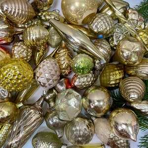 May include: A collection of vintage glass ornaments in various shapes and sizes, including round, teardrop, and cone shapes. The ornaments are mostly gold and silver with some having a frosted or iridescent finish.