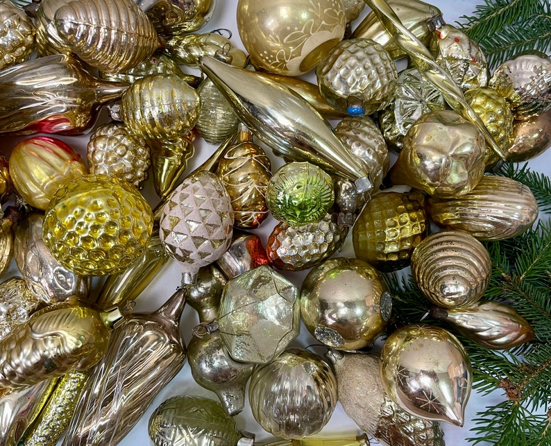 May include: A collection of vintage glass ornaments in various shapes and sizes, including round, teardrop, and cone shapes. The ornaments are mostly gold and silver with some having a frosted or iridescent finish.