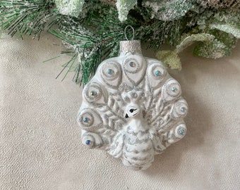 May include: White glass Christmas ornament shaped like a peacock with silver glitter and iridescent accents.