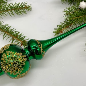 Op de afbeelding: Een groene glazen kerstboomtopper met gouden glitteraccenten. De topper heeft een ronde bolvorm met een puntige top en een lange, dunne steel.