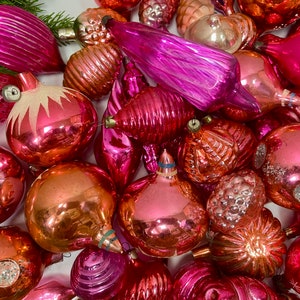 May include: A collection of vintage glass ornaments in various shades of pink and red. The ornaments are all different shapes and sizes, and some have a textured or iridescent finish.