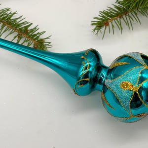 Könnte beinhalten: Blauer Glas-Christbaumspitzen-Anhänger in Türkis mit goldenen Glitzerakzenten und geometrischem Muster.
