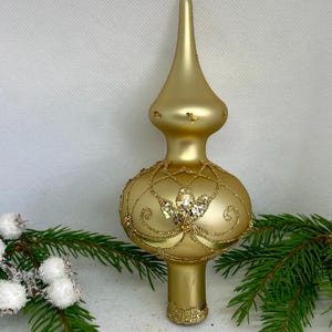 May include: A gold glass Christmas tree topper with a decorative design and glitter accents.