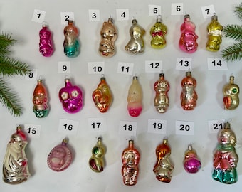 May include: A collection of vintage Christmas ornaments in various shapes and colors, including figures of animals, people, and abstract designs. The ornaments are made of glass and have a shiny, reflective surface.