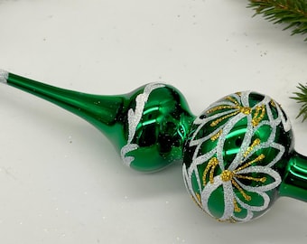Könnte beinhalten: Zwei grüne Christbaumspitzen aus Glas mit weißen und goldenen floralen Designs. Eine Spitze hat eine lange, spitze Spitze mit einem glitzernden weißen Ende. Die andere hat eine runde Form mit einer glitzernden weißen Basis.