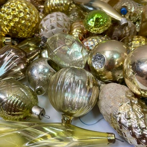 May include: A collection of vintage glass Christmas ornaments in various shapes and sizes, including balls, teardrops, and cones. The ornaments are mostly gold and silver with some clear glass ornaments.