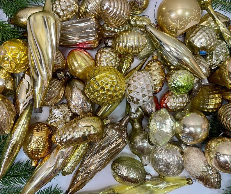 May include: A collection of vintage glass ornaments in various shapes and sizes, including stars, bells, and cones. The ornaments are all silver and gold in color and have a frosted finish. They are perfect for adding a touch of vintage charm to your Christmas tree.