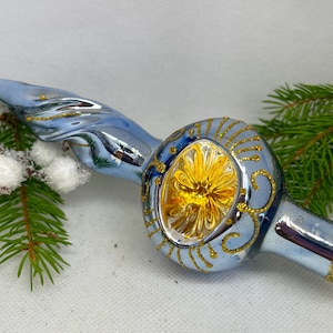 May include: A blue glass Christmas tree topper with a gold swirl design and a yellow glass center. The topper has a pointed end and a round bulb shape.