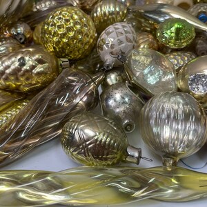 May include: A collection of vintage glass Christmas ornaments in gold, silver, and green. The ornaments are various shapes, including round, teardrop, and icicle. Some ornaments have a textured surface, while others are smooth.