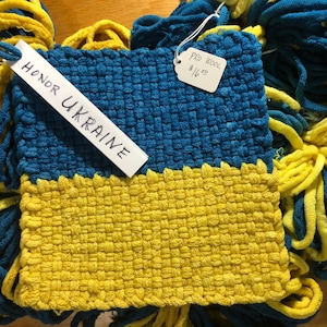 May include: A woven tapestry in the colors of the Ukrainian flag, blue and yellow, with a tag that reads "HONOR UKRAINE".