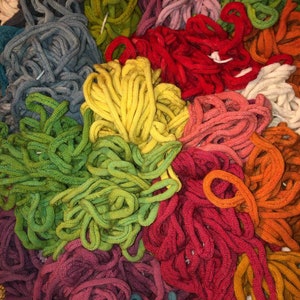 May include: A collection of colorful yarn in various shades of green, red, yellow, orange, blue, and purple. The yarn is arranged in a pile, with some strands overlapping.