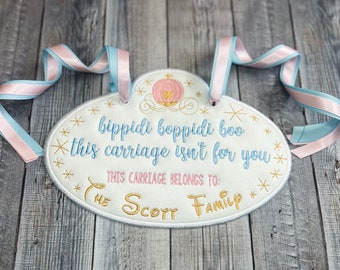 May include: Embroidered oval sign with the text "bippidi boppidi boo this carriage isn't for you". The sign features a pink and blue ribbon for hanging and a pumpkin carriage design. The text "THIS CARRIAGE BELONGS TO: THE SCOTT FAMILY" is also embroidered.