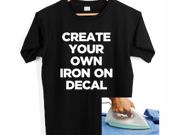 May include: Black t-shirt with white text that reads "CREATE YOUR OWN IRON ON DECAL". An iron is shown ironing a blue fabric.