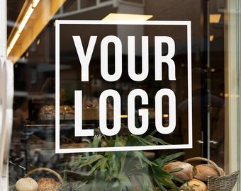 May include: A storefront window with a sign that says "YOUR LOGO" in white text on a black background. There are baskets of bread and a green plant in the window.