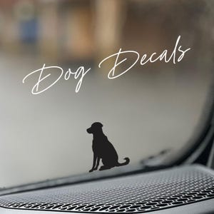 May include: Black silhouette of a dog sitting, with the words "Dog Decals" in cursive script above. The decal is designed for application on a car window or similar surface.