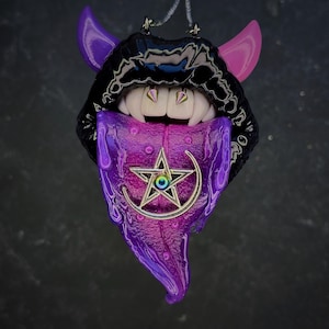 May include: A unique pendant featuring a stylized mouth with fangs, purple tongue, and horns. The mouth is black with pink and purple accents. The tongue has a silver pentagram and crescent moon design. The pendant has a glossy finish.