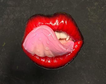 Könnte beinhalten: Nahaufnahme eines roten Mundes mit einer herausgestreckten rosa Zunge. Die Lippen sind glänzend und die Zunge ist feucht.