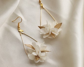 May include: A pair of gold dangle earrings with white flower accents. The earrings feature a delicate triangle shape and are adorned with small, white paper flowers.
