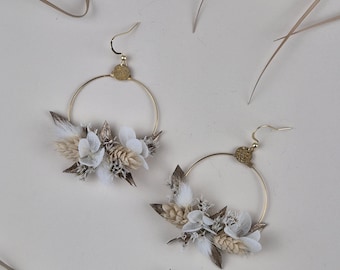 May include: A pair of gold hoop earrings with dried flowers and feathers. The flowers are white and beige, and the feathers are white.