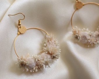 May include: A pair of gold hoop earrings with a delicate floral design. The hoops are adorned with small, dried white flowers.