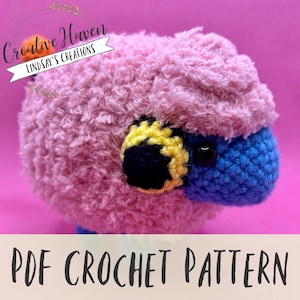 May include: A crochet pattern for a pink and blue sheep with a yellow and black eye. The pattern is available as a PDF download.  "Creative Haven Lindsay's Creations" is written on a white banner with green leaves.
