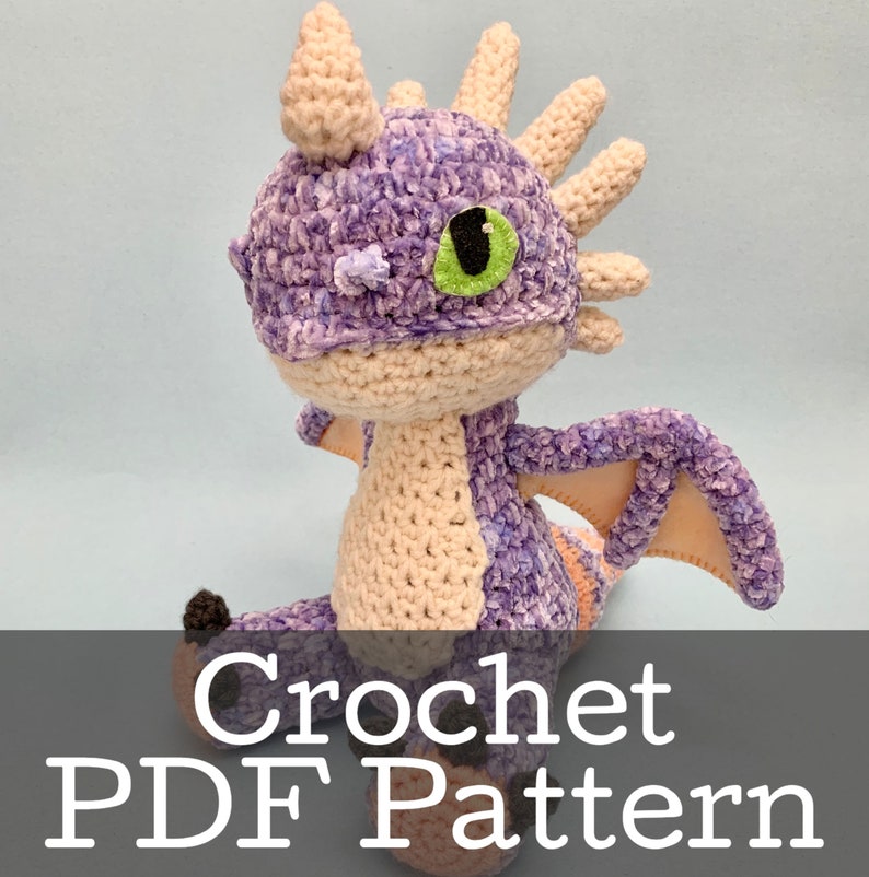 Peut inclure: Patron de crochet PDF pour un amigurumi de dragon violet et cr&egrave;me. Le dragon a un &oelig;il vert et une cr&ecirc;te en cr&egrave;me h&eacute;riss&eacute;e.