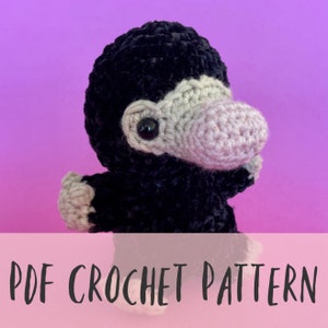 May include: A handmade crochet creature with a black body, gray face, and light gray accents. The creature has a rounded head, a prominent nose, and small arms. The text "PDF CROCHET PATTERN" is displayed at the bottom of the image.