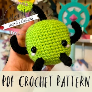 Puede incluir: Un patrón de crochet para una criatura amigurumi verde y negra con ojos grandes. El patrón está disponible para descargar en PDF.  PDF CROCHET PATTERN.