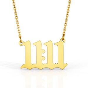 May include: A gold-colored necklace with a chain and a pendant featuring the number 1111 in a gothic font. The pendant is centered and reflects light, set against a white background.