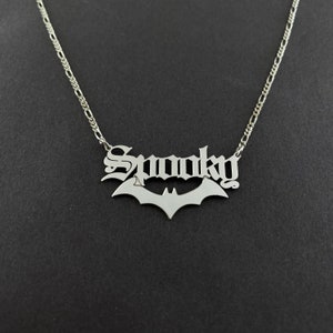 以下が含まれることがあります： ゴシック体で「Spooky」と書かれたバットペンダントが付いたシルバーネックレス