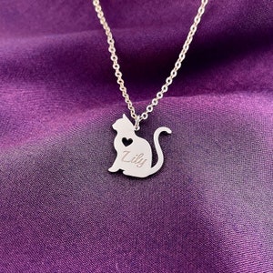 Pode incluir: Colar de prata com um pingente com a silhueta de um gato. O pingente tem um pequeno cora&ccedil;&atilde;o recortado e o nome "Lily" gravado.